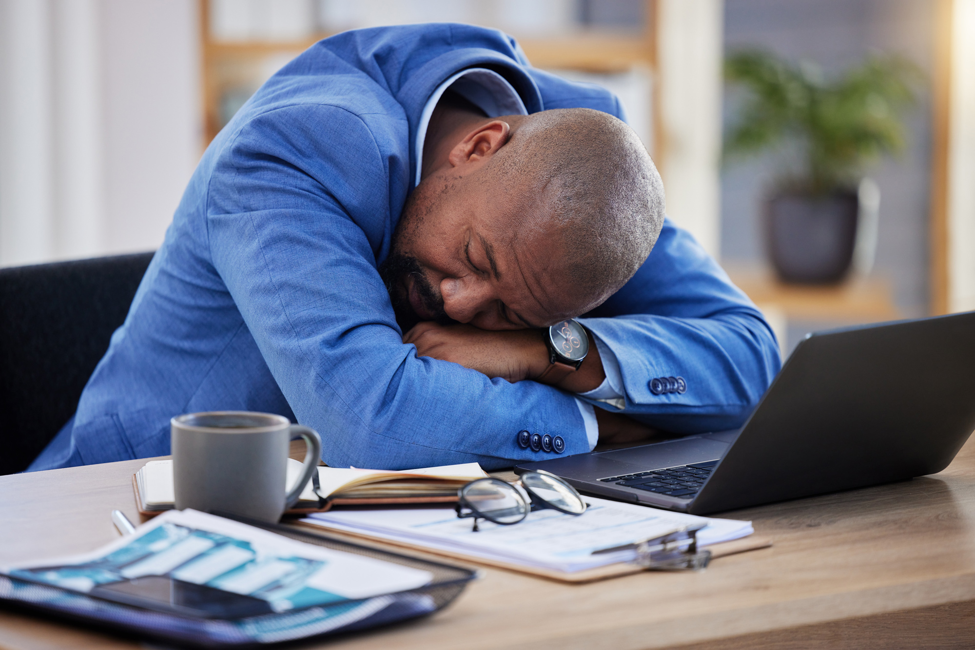 stresses man rests his head in his arms on his office desk